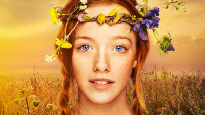 Anne's face is centered and takes up most of the frame. Her red hair is in two braids with one over each shoulder. She's wearing a flower crown and her eyes are a bright blue.
