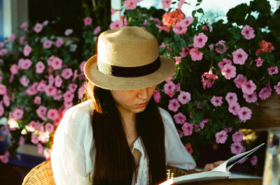Woman with a staw hat on reading a book outside in front of annuals.