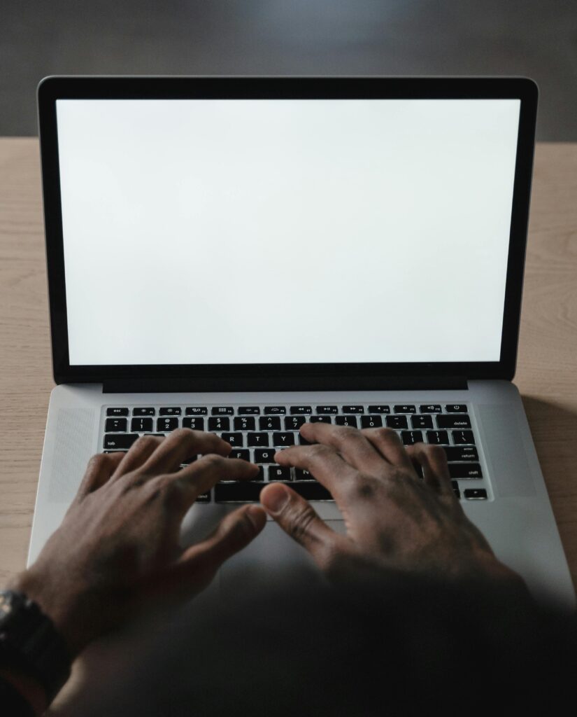 Photograph of a laptop with a blank page on it and hands ready to type.