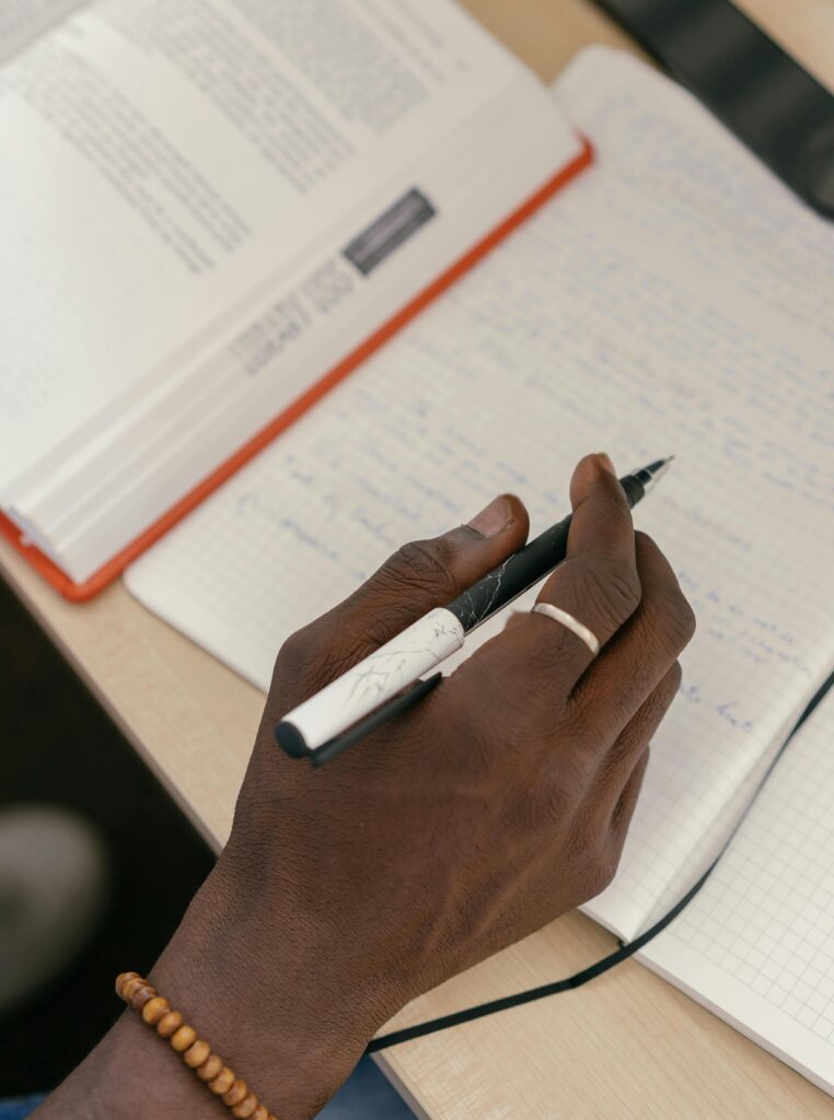Photograph of a hand holding a pen about to write on an open notebook.